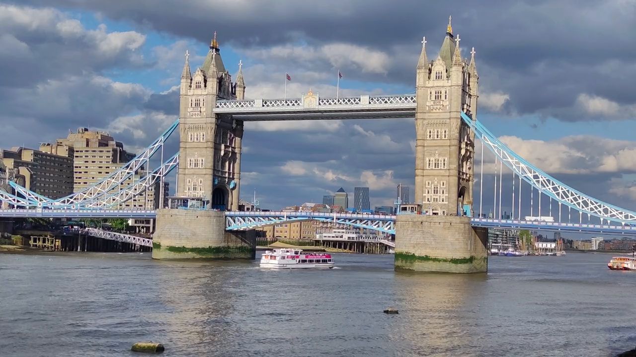 Tower Bridge and its blue suspension chains over the Thames, with a small boat on the river
