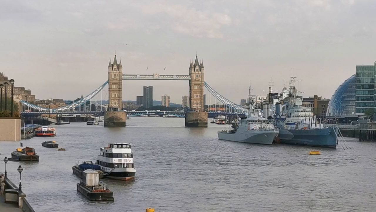 Tower Bridge in the distance, with a grey warship and small boats on the river in front
